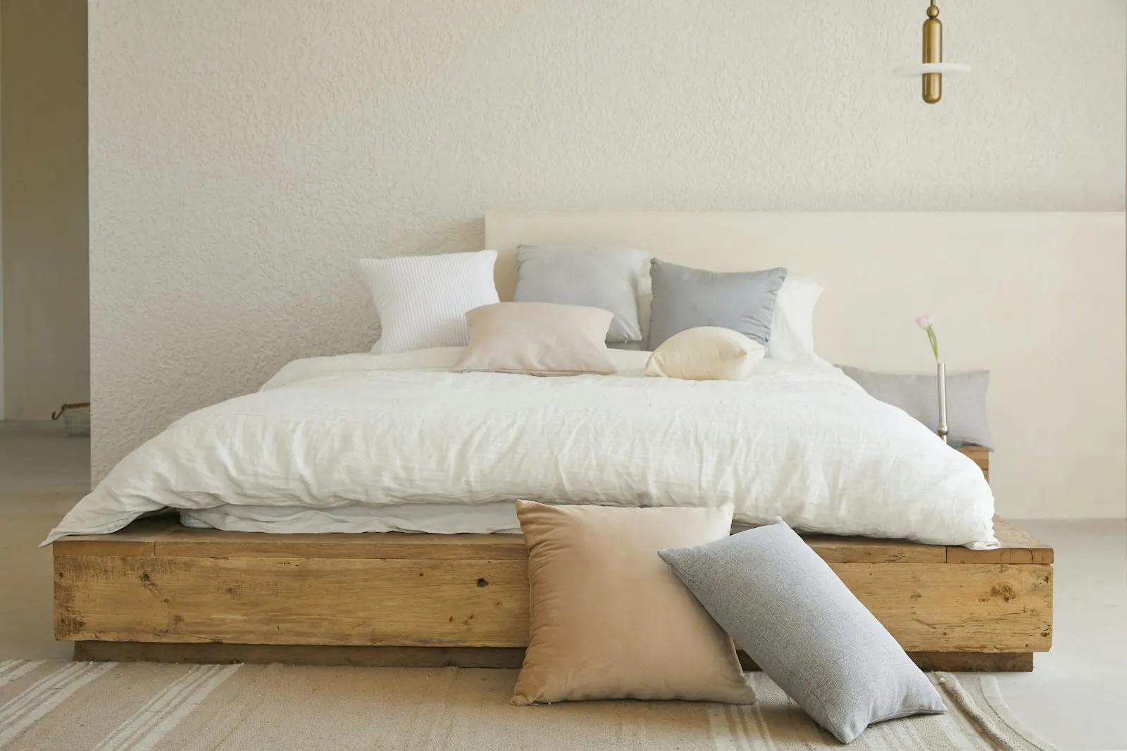 Slaapkamer met een bed van ruw eikenhout, linnen in zand en lichtgrijs, en een messing hanglamp tegen een kalkpleistermuur