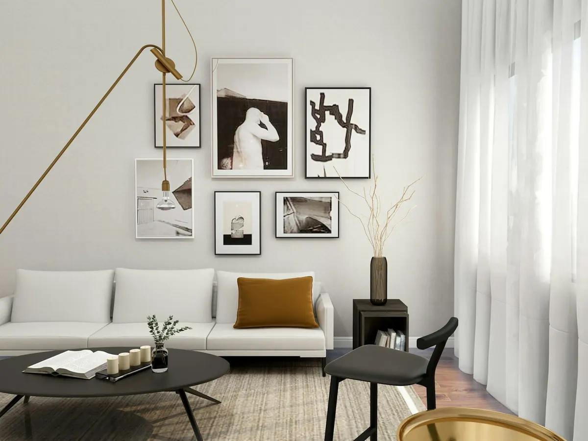 Lichte woonkamer met een witte sofa, een okergeel kussen, een messing vloerlamp en een wand vol ingelijste tekeningen