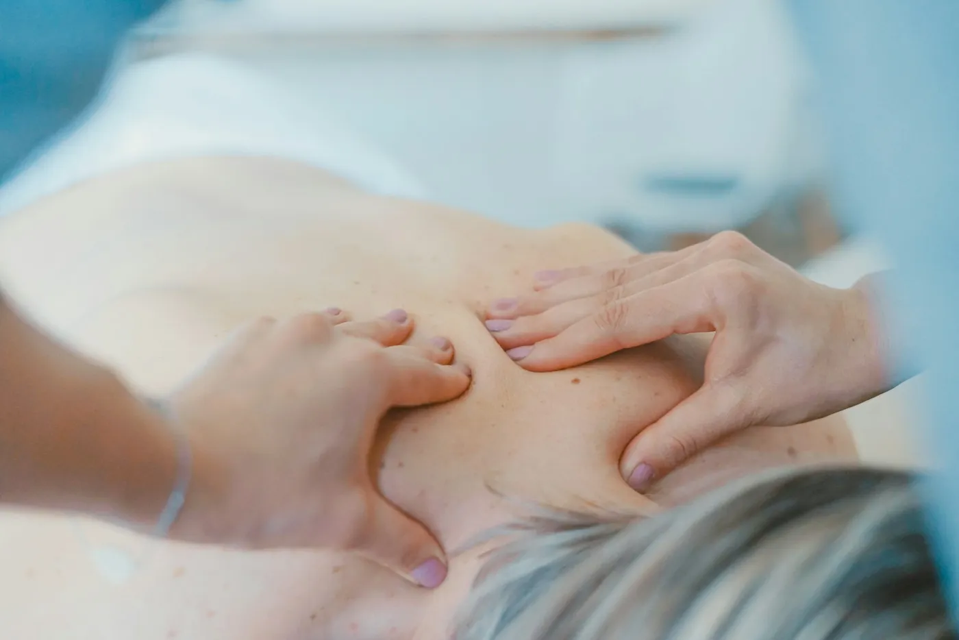 Handen van een kinesitherapeute tijdens een behandeling van de schouders
