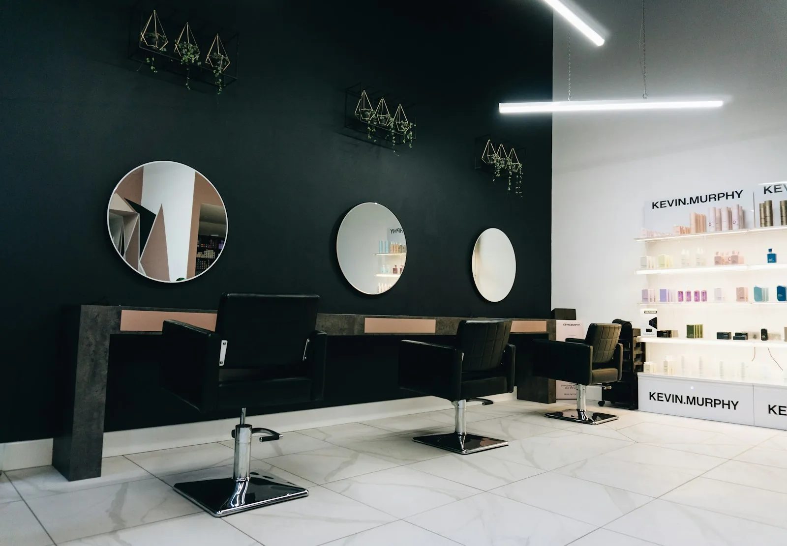 Het salon van Studio Kapsel: donkere muren, ronde spiegels en zwarte kappersstoelen
