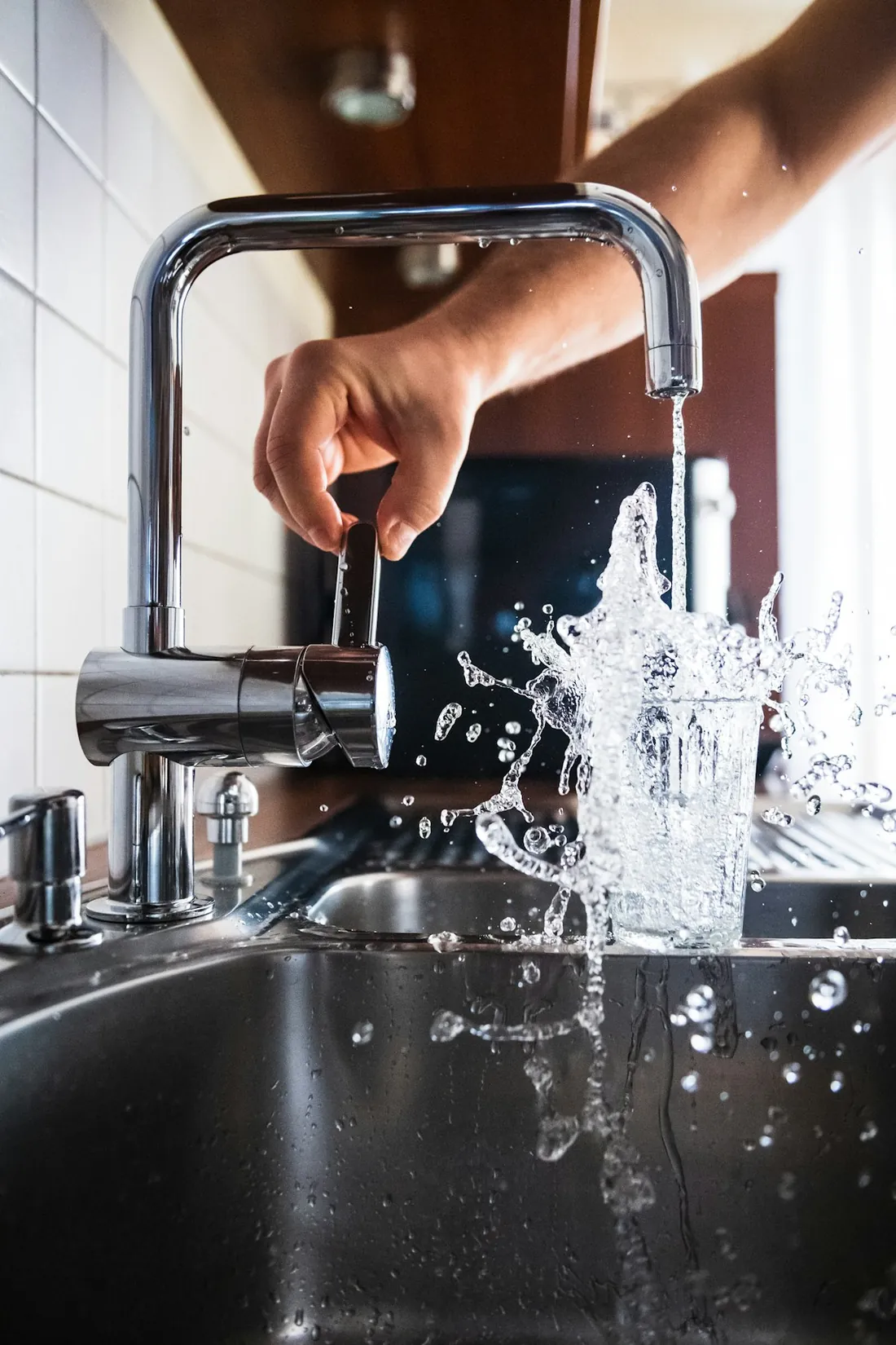 Een hand opent een chromen keukenkraan, het water spat in de spoelbak
